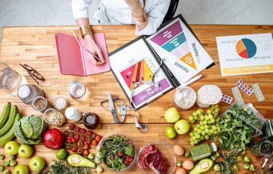 Dietitian writing diet plan, view from above on the table with different healthy products and drawings on the topic of healthy eating